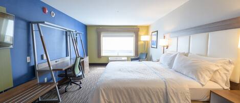 A hotel room with a large bed, a desk, a chair, a TV, and a window with blinds.