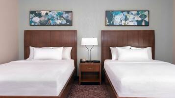 A hotel room with two beds, a nightstand with a lamp, and floral artwork on the walls.