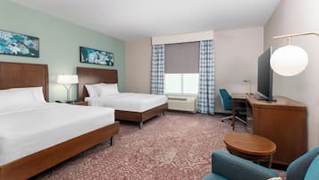 A hotel room with two beds, a desk, a chair, a TV, and artwork on the walls.