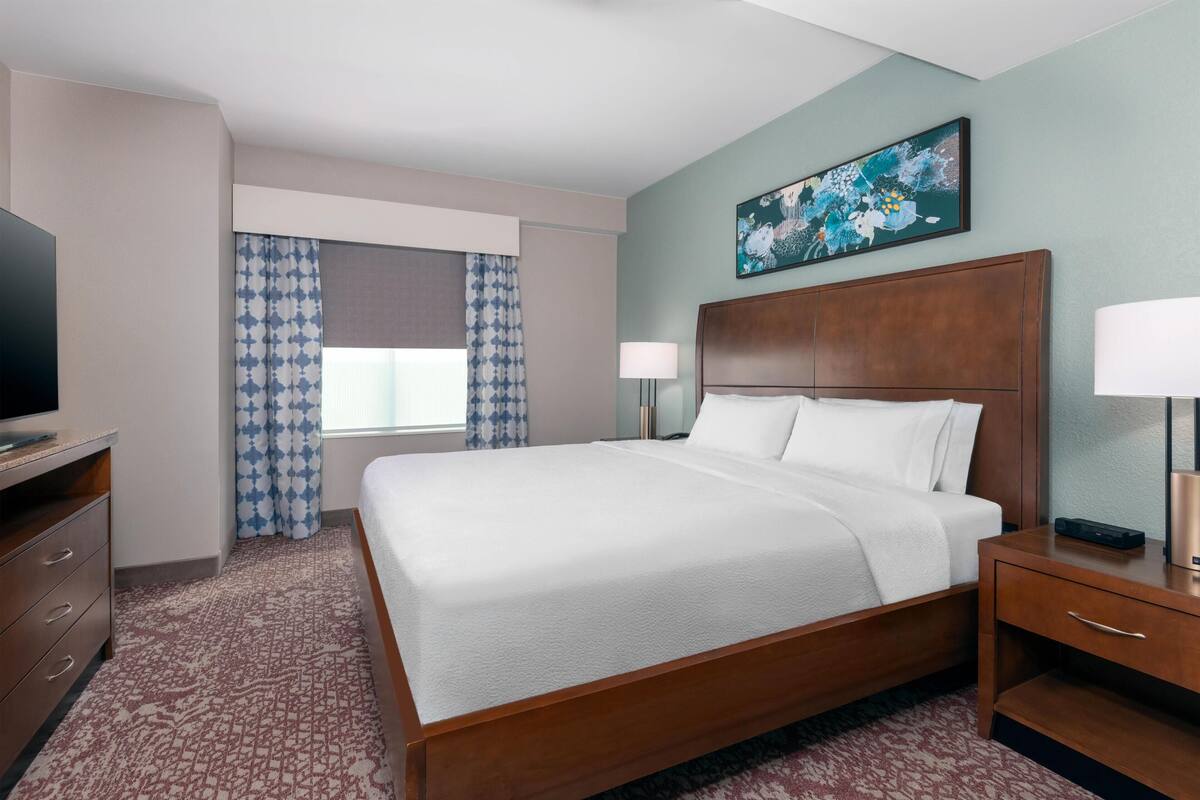 Habitación de hotel con una cama grande, televisor, escritorio y ventana con cortinas.