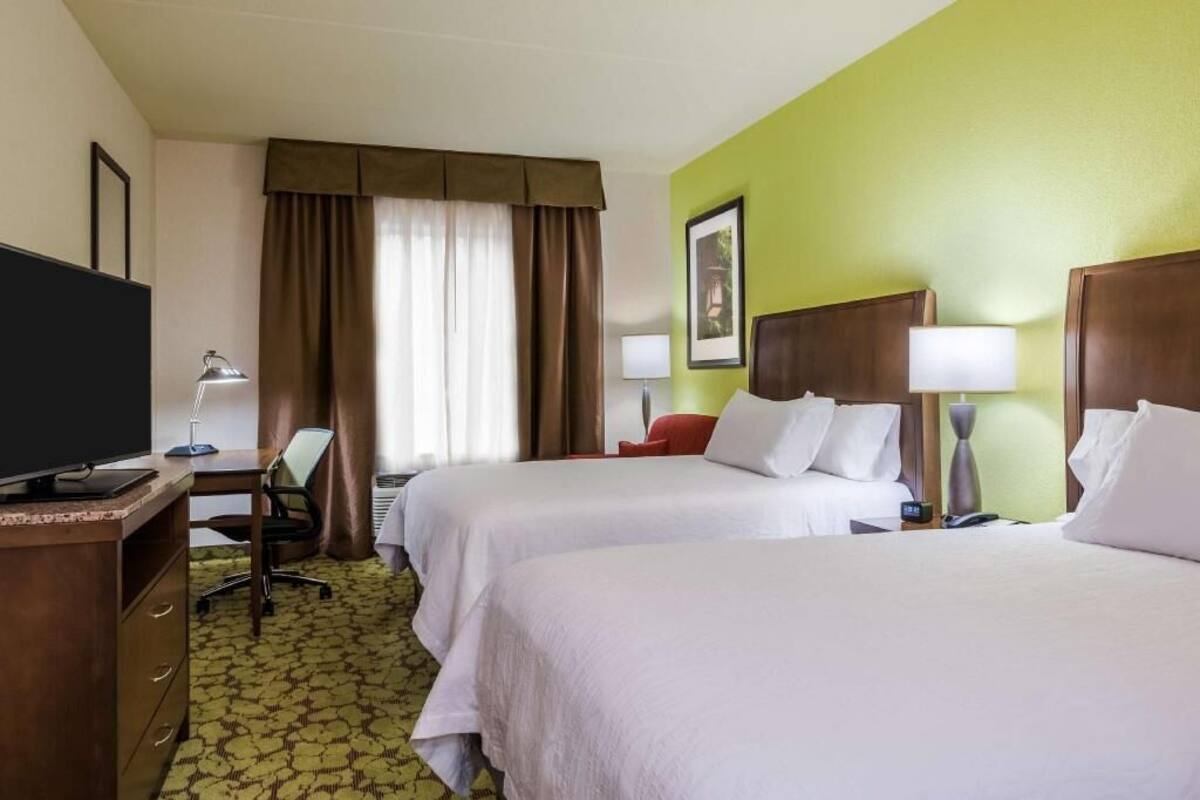 Habitación de hotel con dos camas, un escritorio, una computadora, un televisor y una lámpara.