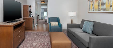 Una sala de estar moderna con una televisión de pantalla plana, un sofá, un sillón azul, un mueble de madera y una alfombra estampada.