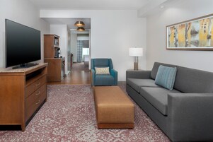 Una sala de estar moderna con una televisión de pantalla plana, un sofá, un sillón azul, un mueble de madera y una alfombra estampada.