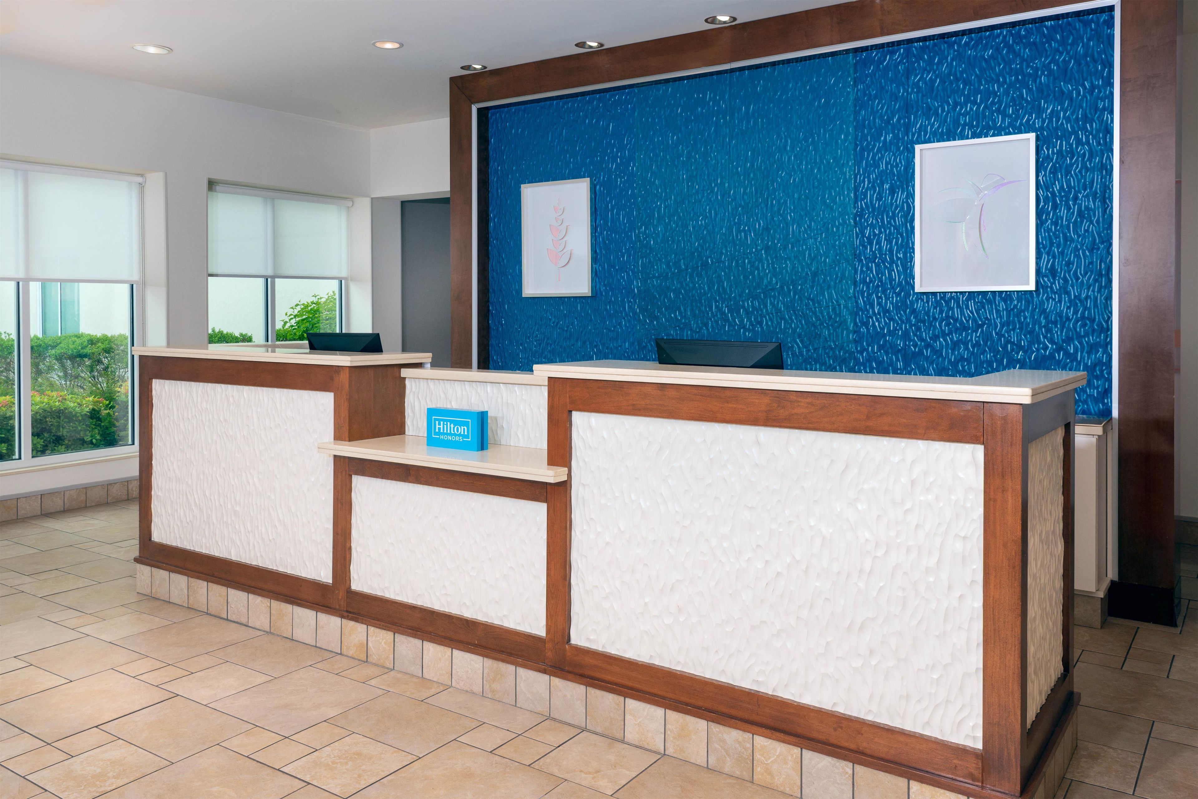 A hotel reception desk with a blue textured wall, framed artwork, and a 'Hilton' sign.