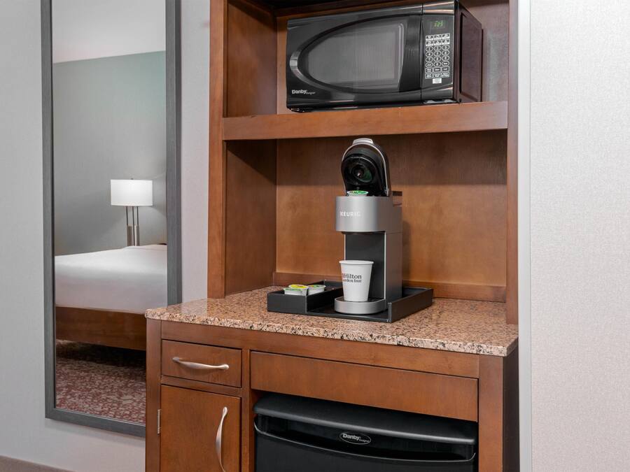 Een kitchenette met een magnetron, een Keurig koffiezetapparaat en een koffiekop met het Hilton logo.