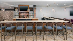 Zona de bar moderna con una barra larga, varios taburetes y lámparas colgantes.