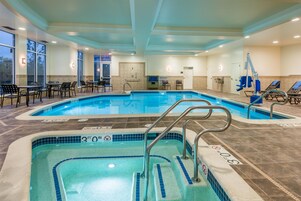 An indoor swimming pool with multiple lanes, a hot tub, and lounge chairs.
