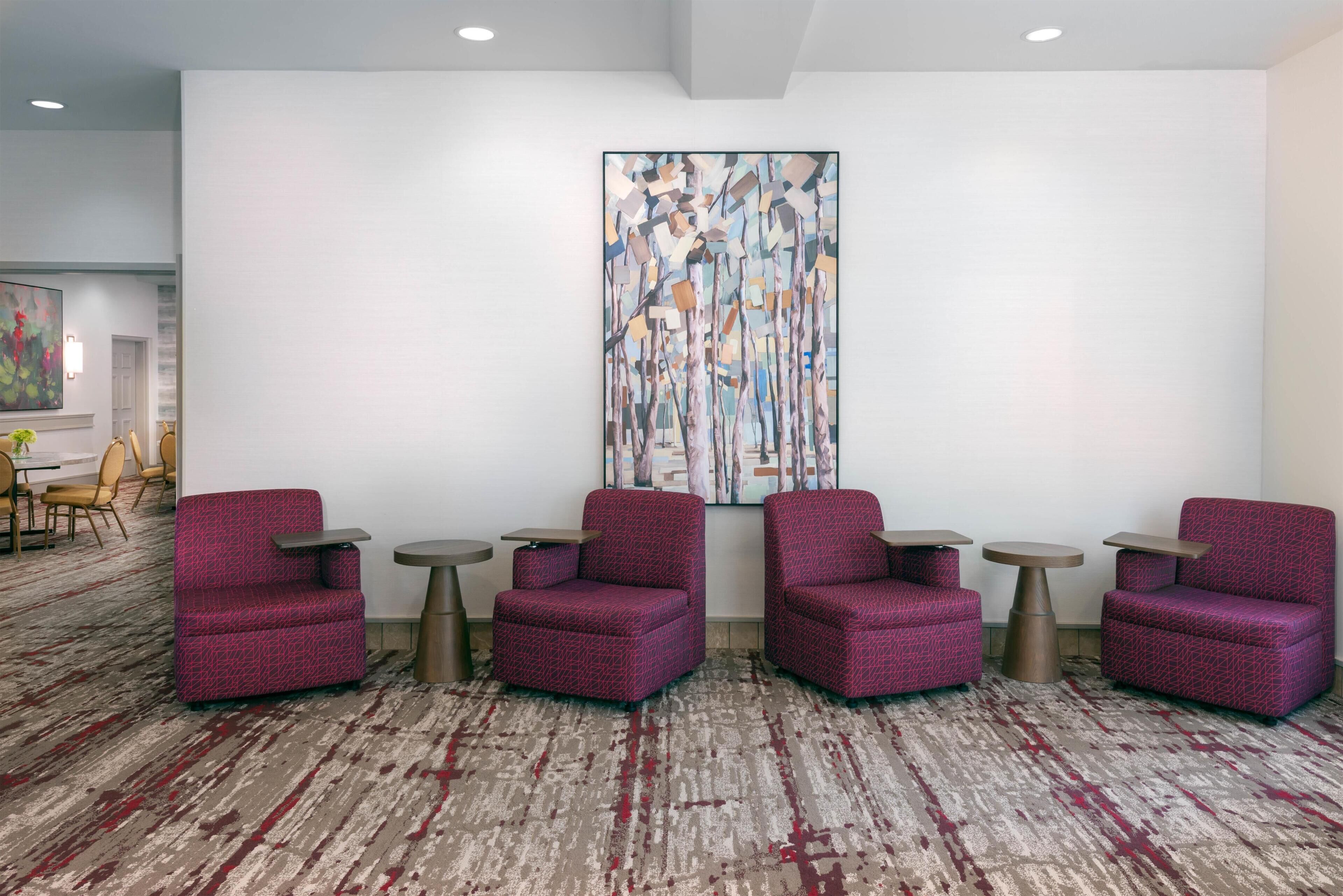 A lobby with four red armchairs, small round tables, and a large abstract painting on the wall.