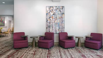 A lobby with four red armchairs, small round tables, and a large abstract painting on the wall.