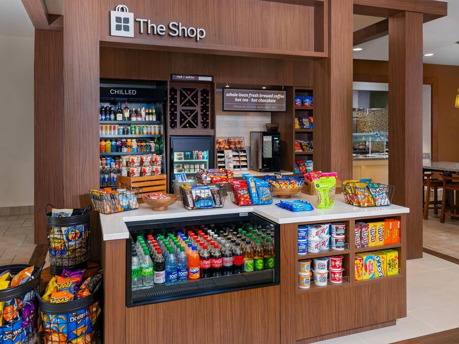 A snack and beverage kiosk in a shopping area with a variety of snacks, drinks, and a coffee machine.