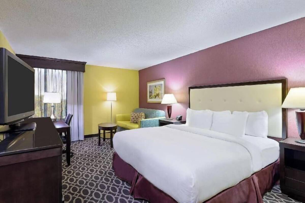Habitación de hotel con una cama grande, un escritorio con televisor, una silla, una mesita y una lámpara.
