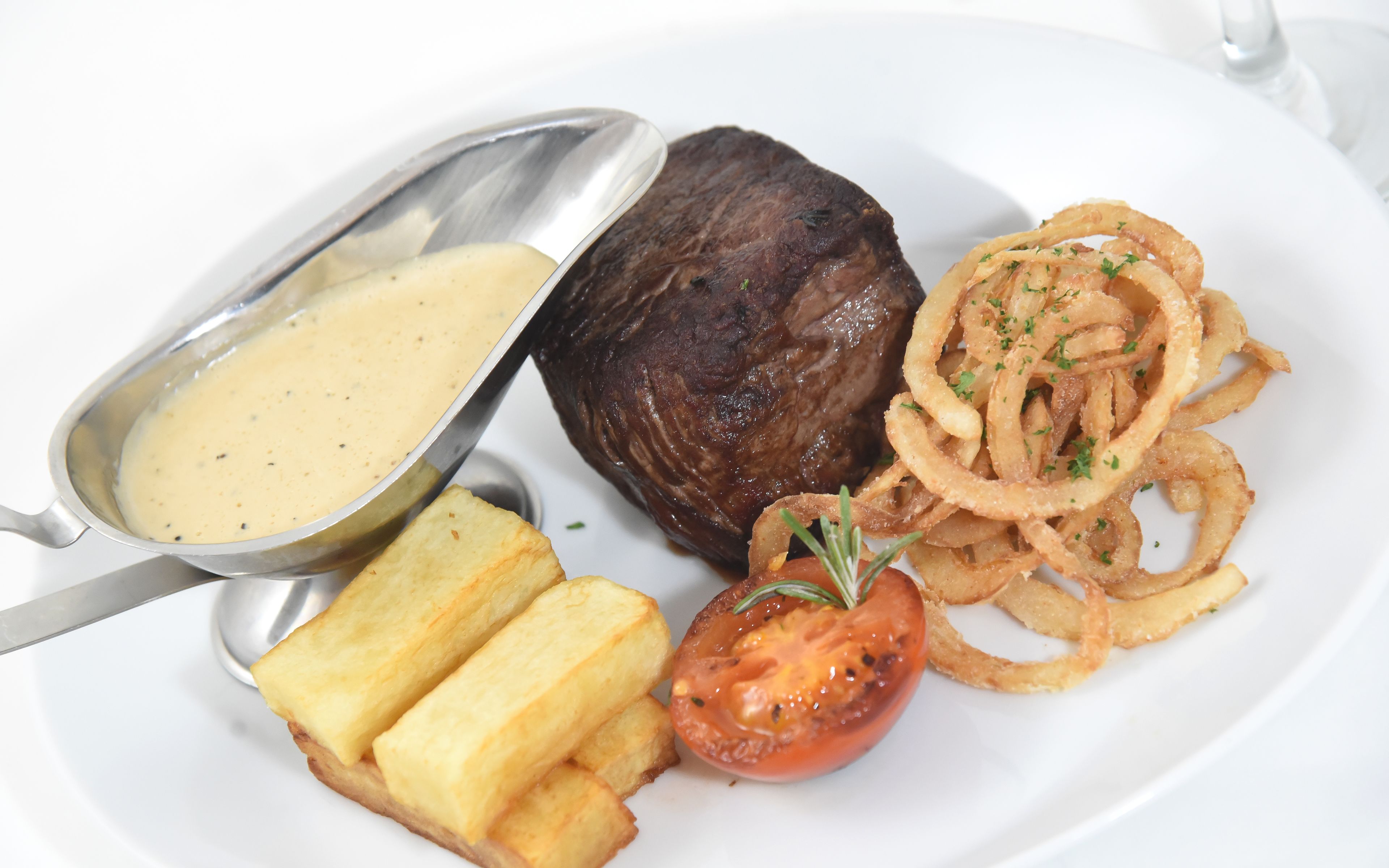 A plate with steak, onion rings, a tomato, and a side of mashed potatoes.