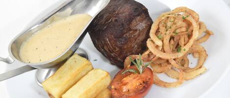 Une assiette comprenant un steak, des rondelles d’oignon, une tomate et une portion de purée de pommes de terre.