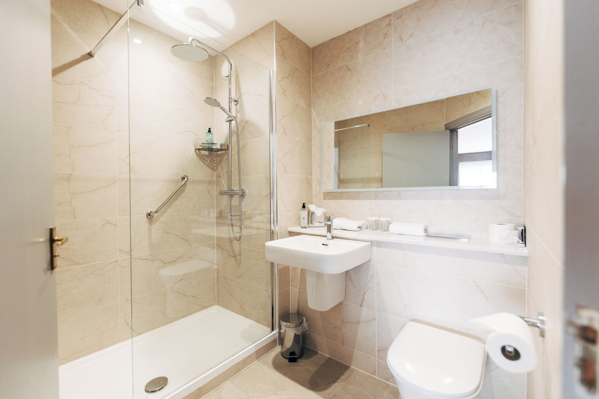 A modern bathroom with a glass-enclosed shower, a pedestal sink, a toilet, and a mirror above the sink.
