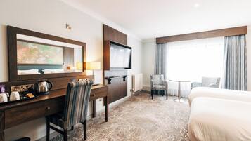 Habitación de hotel con cama, escritorio, silla, televisor y un ventanal con cortinas.