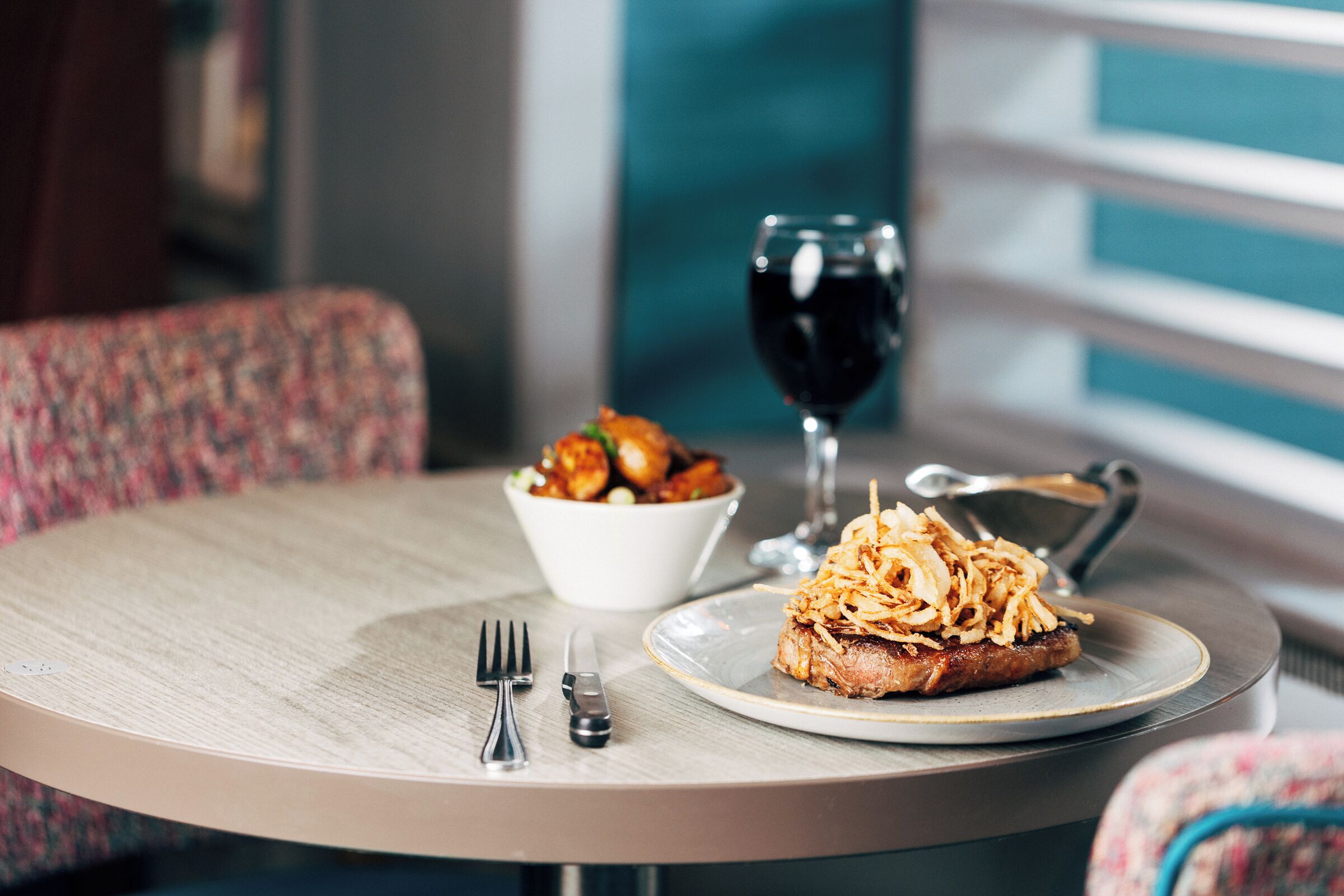 A round table with a plate of food, a bowl of salad, a glass of red wine, and cutlery.