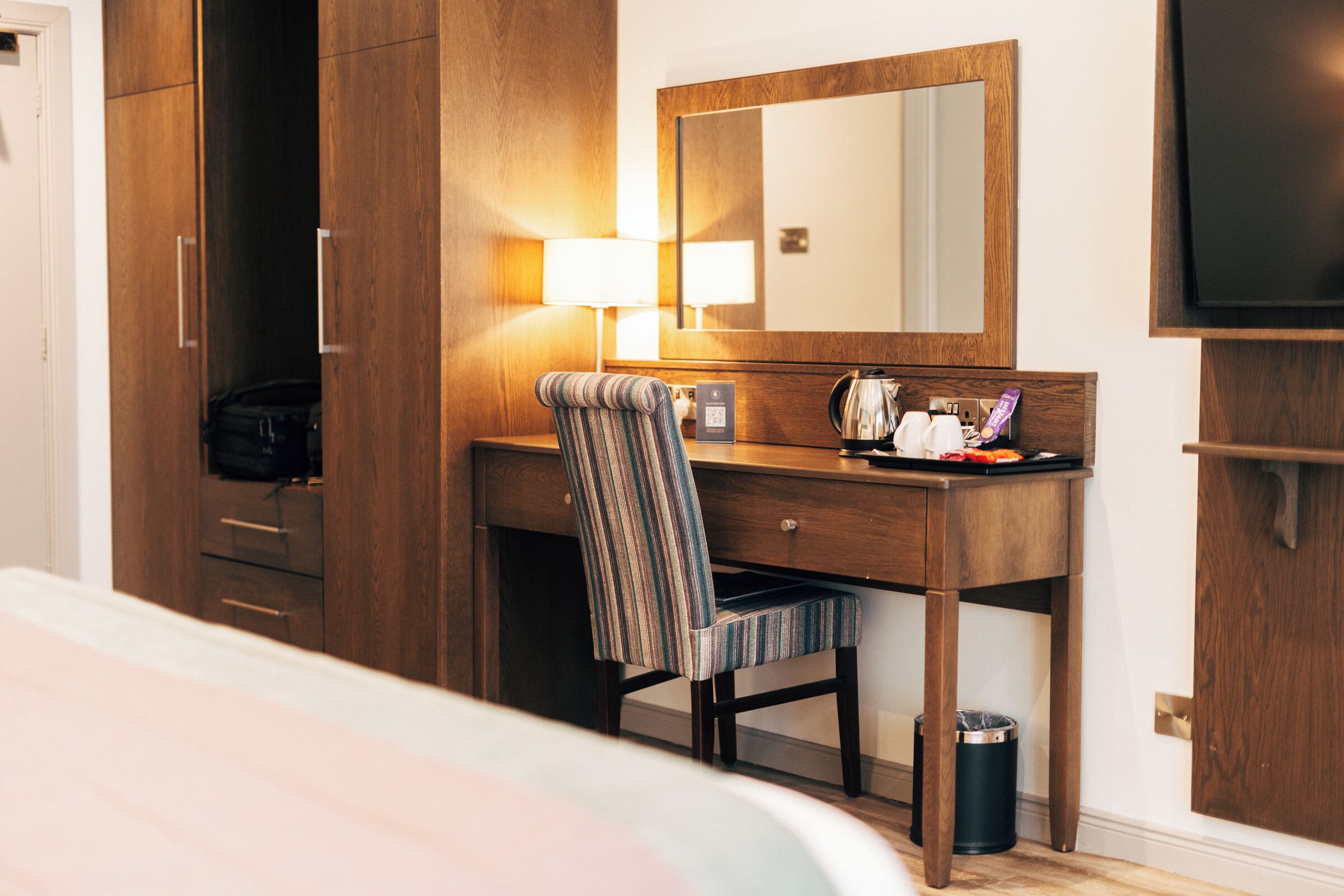 A hotel room with a wooden desk, a chair, a television, and a bed.