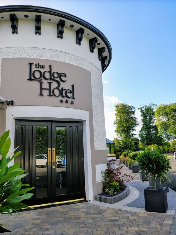 Fasaden på The Lodge Hotel är böjd, och hotellet har en svart entrédörr samt en skylt ovanför dörren.