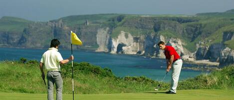 Dos personas jugando golf en un campo con vistas al mar.