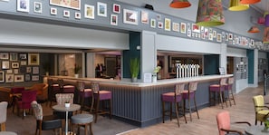 A bar area with a counter, multiple seating options including bar stools and chairs, and a wall adorned with framed pictures.
