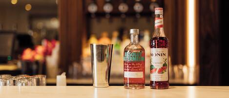 A bar counter with two bottles of Absolut watermelon and Monin, a cocktail shaker, and several glasses.