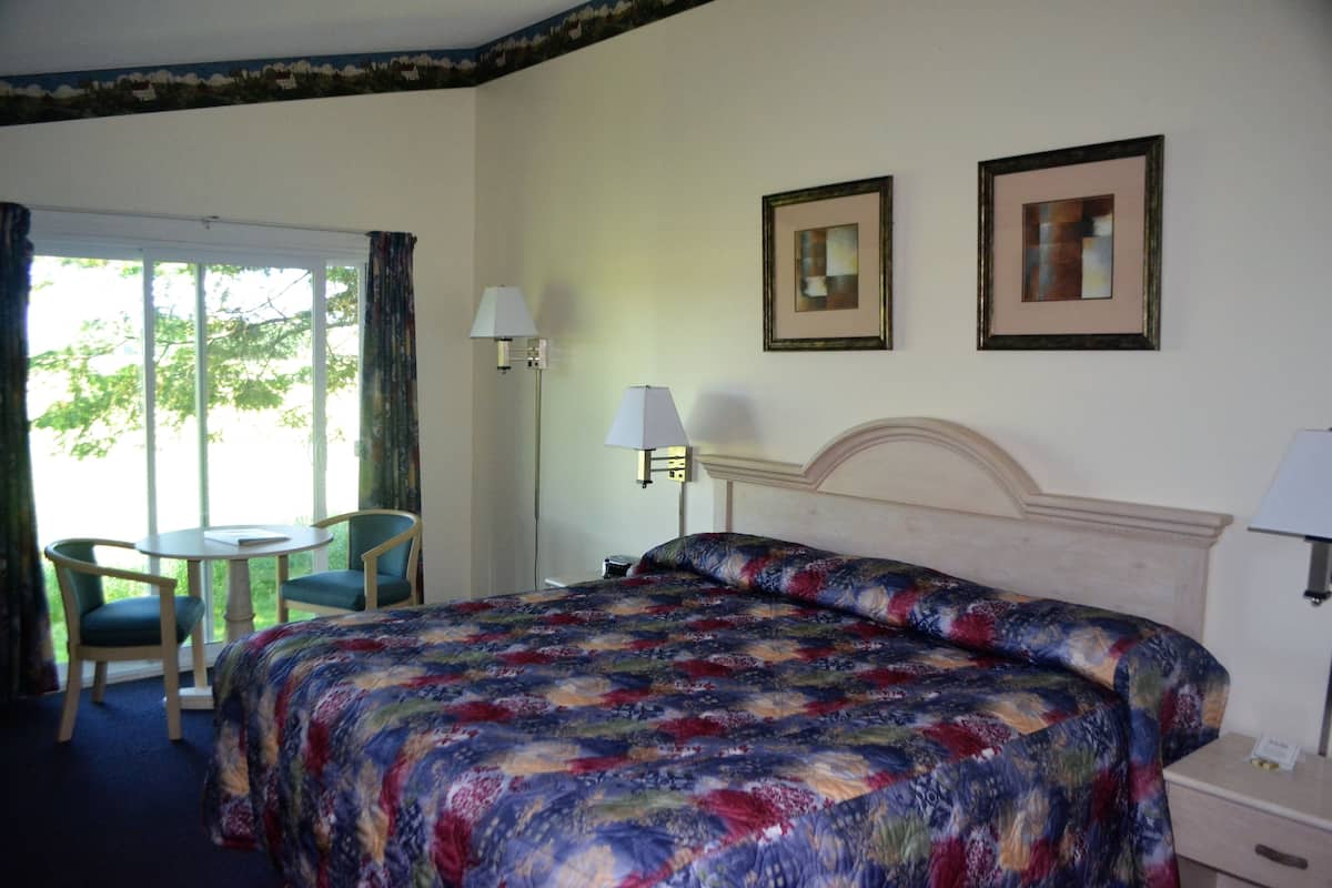 A hotel room with a large bed, a small table with chairs, a window with curtains, and two framed pictures on the wall.
