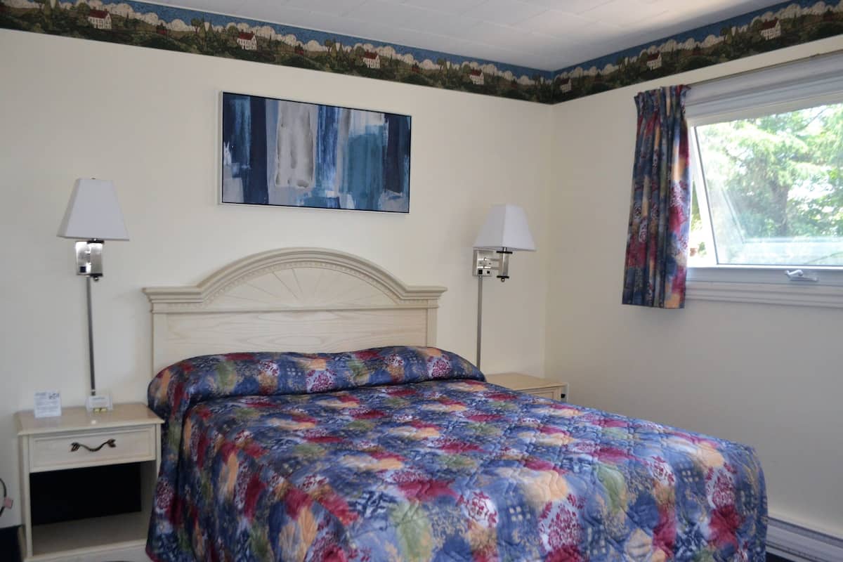 A bedroom with a bed, two bedside tables, a nightstand, a painting on the wall, and a window with curtains.