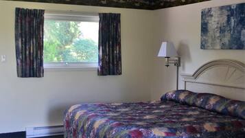 Um quarto com cama, janela com cortinas, abajur e um quadro na parede.