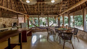 A thatched-roof dining area with a stone wall, a wooden table, and wicker chairs.