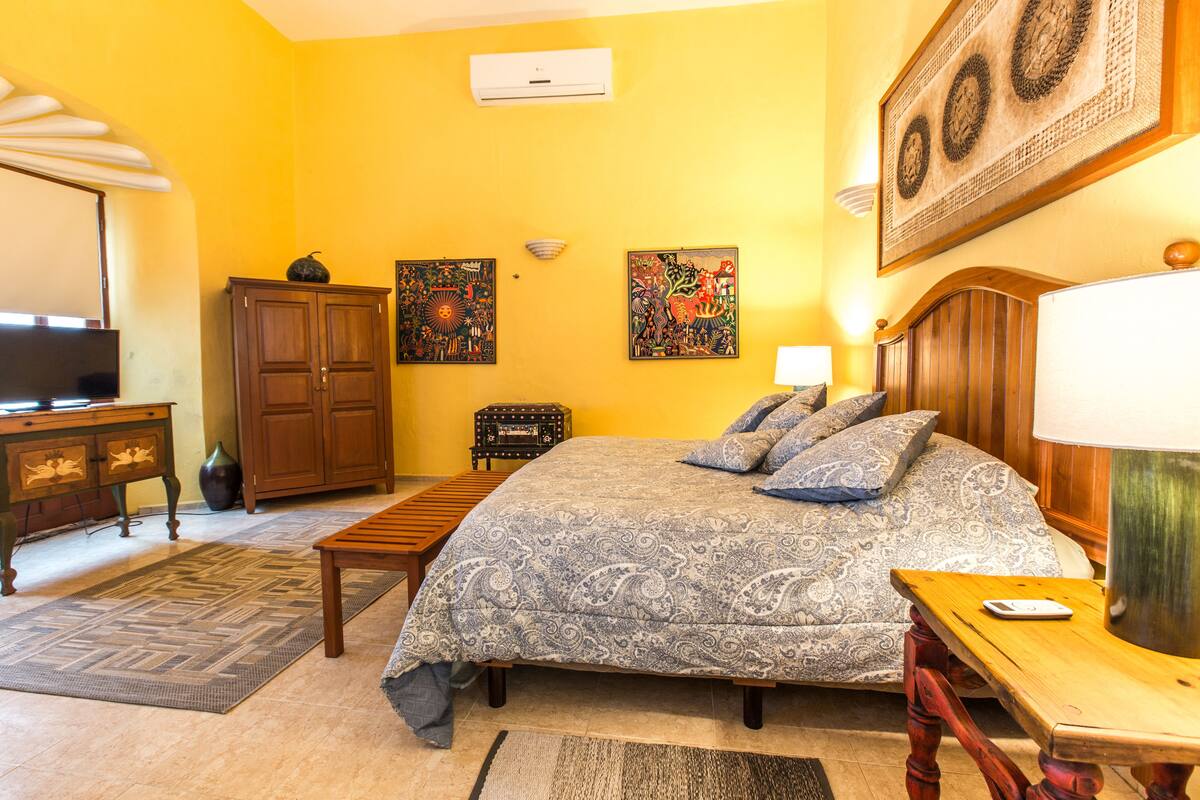 Un dormitorio con cama, escritorio, televisor y obras de arte en las paredes.