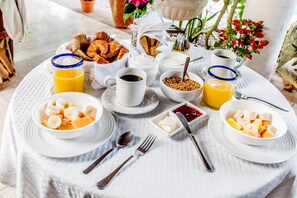 Una mesa de desayuno con diferentes alimentos y bebidas, incluyendo cuencos de fruta, una taza de café y una jarra de jugo de naranja.