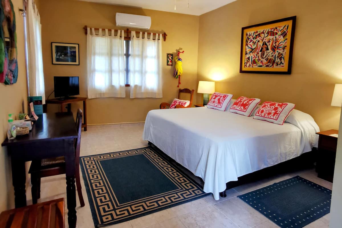 Habitación de hotel con cama, escritorio, silla, ventilador de techo y ventana con cortinas.