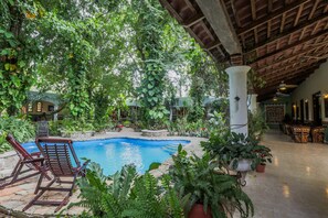 Ein Poolbereich mit Liegestühlen, Topfpflanzen und einer überdachten Terrasse.
