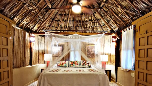 A room with a bed, a woven ceiling, and a patterned rug.