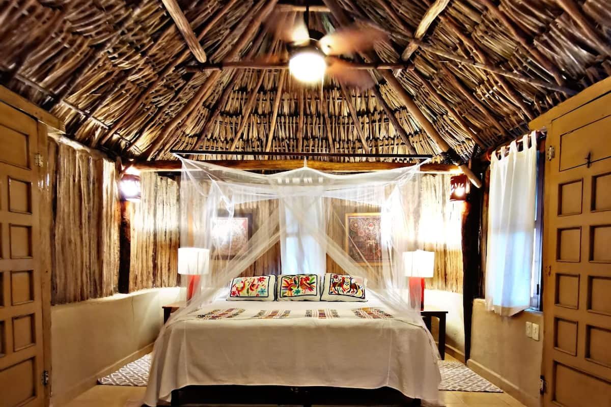 Una habitación con cama, techo tejido y alfombra estampada.