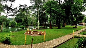 A lush garden with a pond, wooden chairs, and a stone pathway. - Pulhapanzak Waterfalls Cabins (San Francisco de Yojoa)