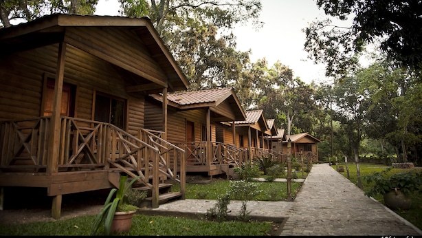 A row of wooden cabins with balconies, surrounded by greenery and a stone pathway. - Pulhapanzak Waterfalls Cabins (San Francisco de Yojoa)