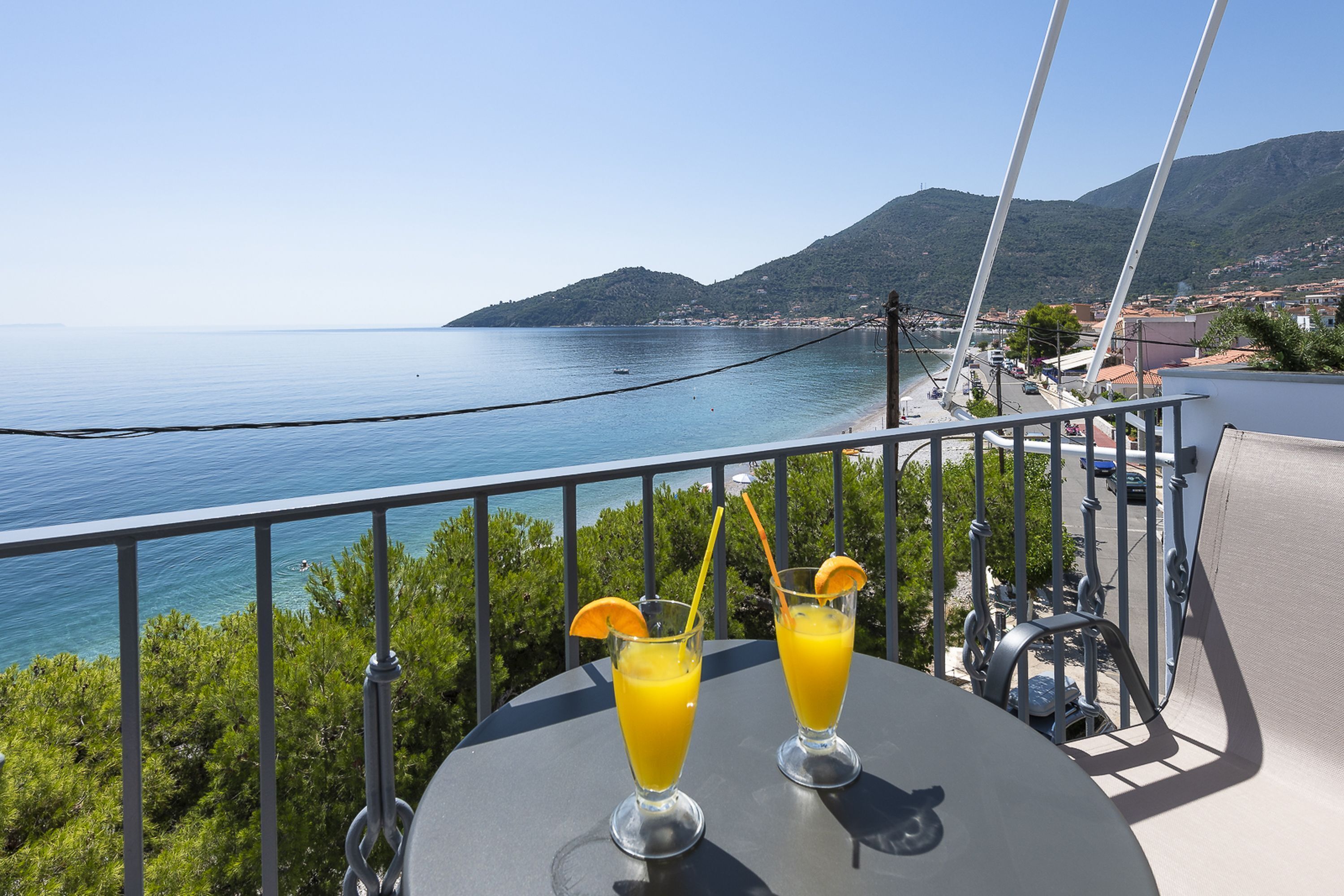 Un balcone con due bicchieri di succo d'arancia, una ringhiera e vista sul mare e sulle montagne.