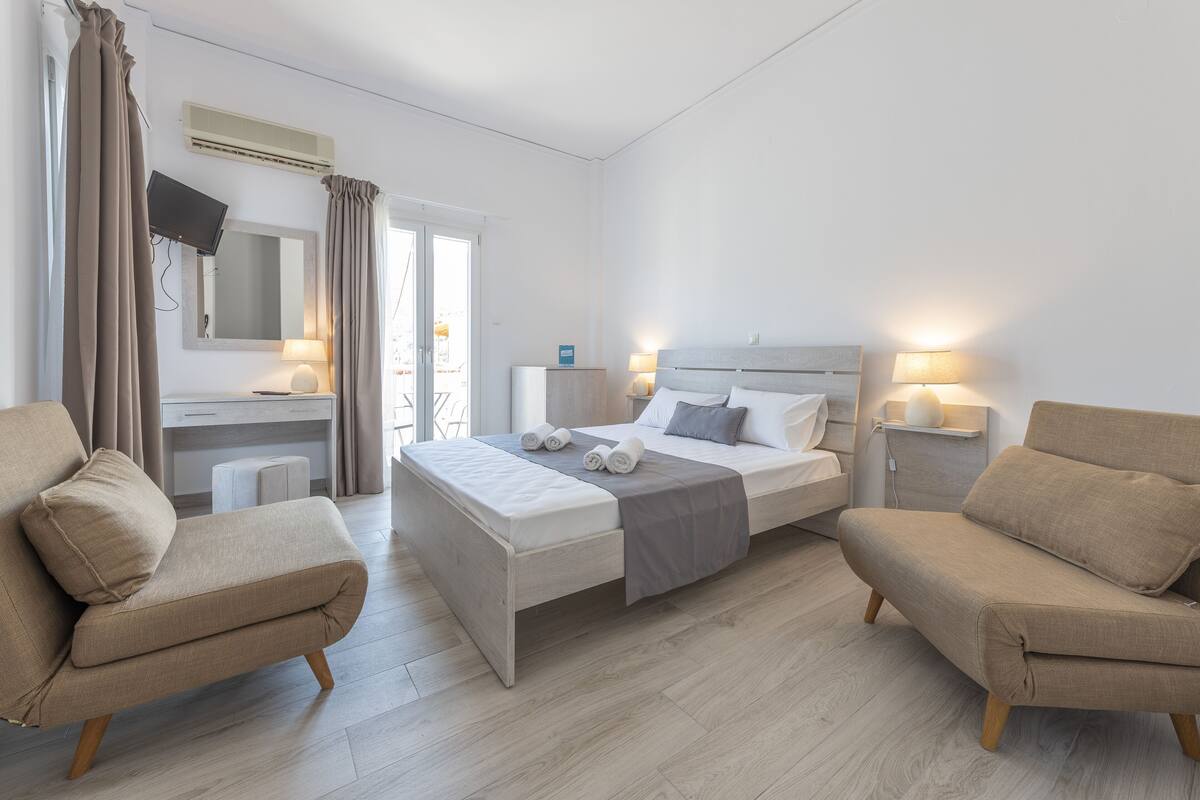 Une chambre d’hôtel moderne équipée d’un lit, de deux fauteuils, d’un bureau et d’une télévision.