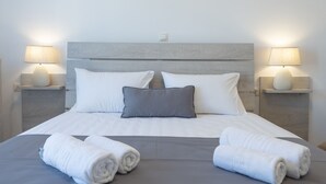 A neatly made bed with white and gray linens, two bedside lamps, and a night switch on the headboard.