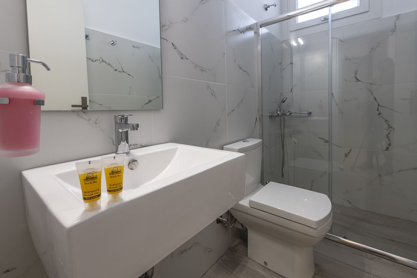 Un baño con lavamanos blanco, inodoro y ducha con mampara de vidrio.