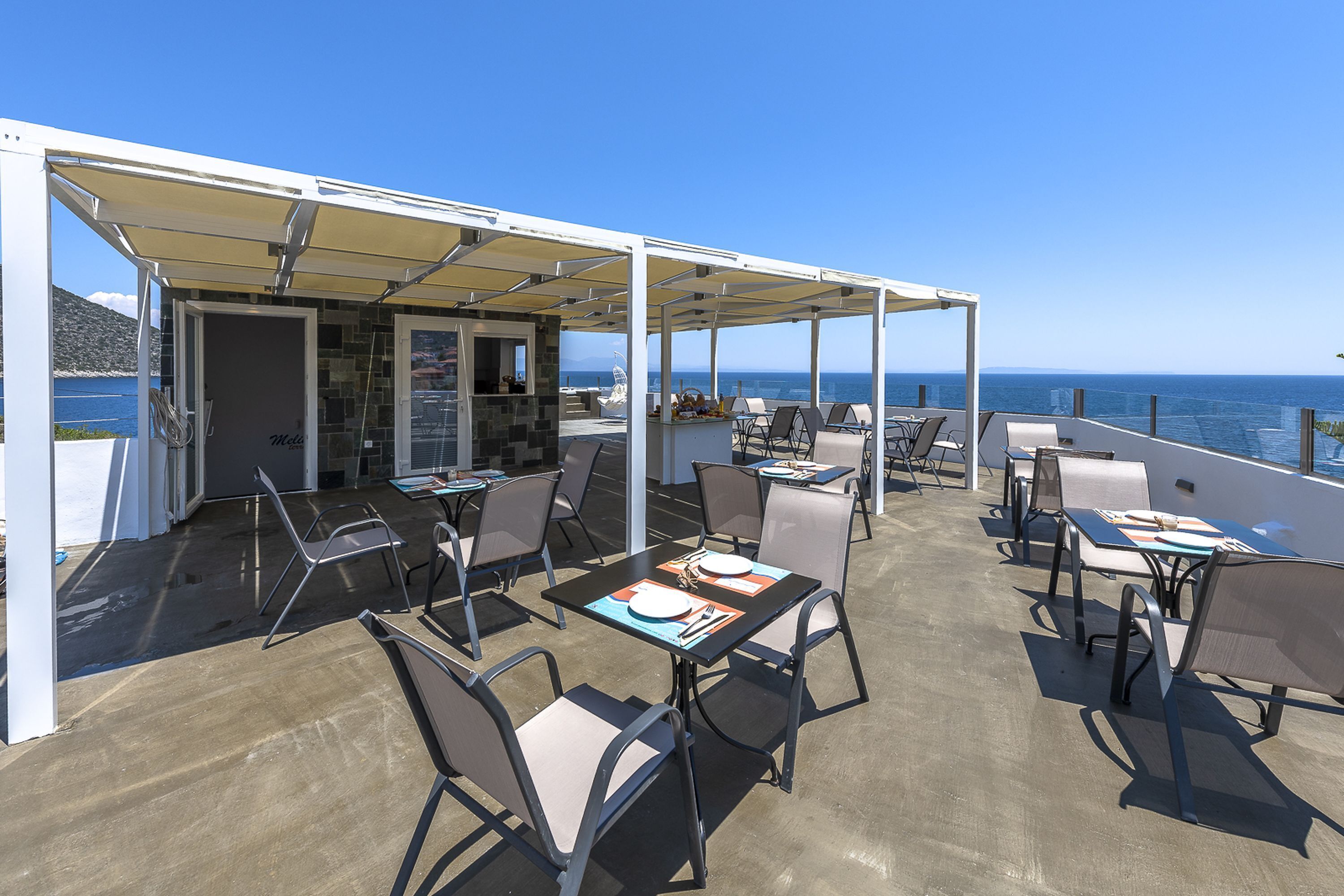Un espace extérieur aménagé pour les repas, avec des tables et des chaises, un coin salon abrité et une vue sur la mer.