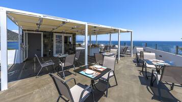 Un espace extérieur aménagé pour les repas, avec des tables et des chaises, un coin salon abrité et une vue sur la mer.