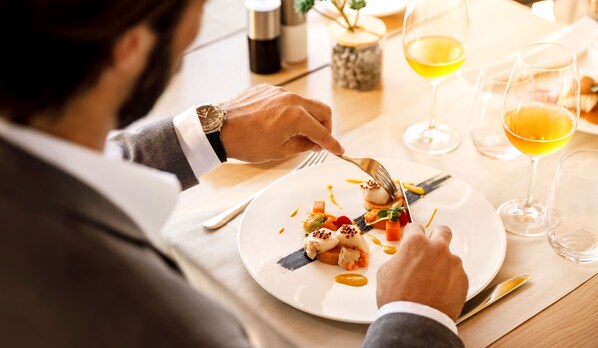A person dining at a table with a white plate of food, a fork, and a knife. There are two glasses of wine on the table. - Isabella Island Miramare Suites - Villas, Valamar Collection (Porec)