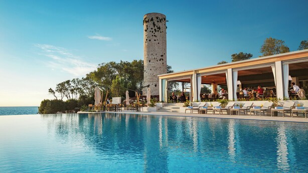 A pool with lounge chairs, a covered seating area, and a tower in the background. -  Isabella Island Miramare Suites - Villas, Valamar Collection (Porec)