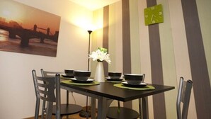Uma sala de jantar com uma mesa posta para quatro pessoas, um vaso de flores e um relógio na parede.