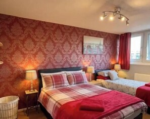 Quarto de hotel com duas camas, papel de parede estampado, uma pintura com vista para a cidade e uma janela com cortinas.