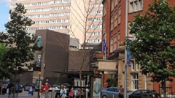 Um hotel com um edifício moderno e alto, e um edifício de tijolos tradicionais com um letreiro.