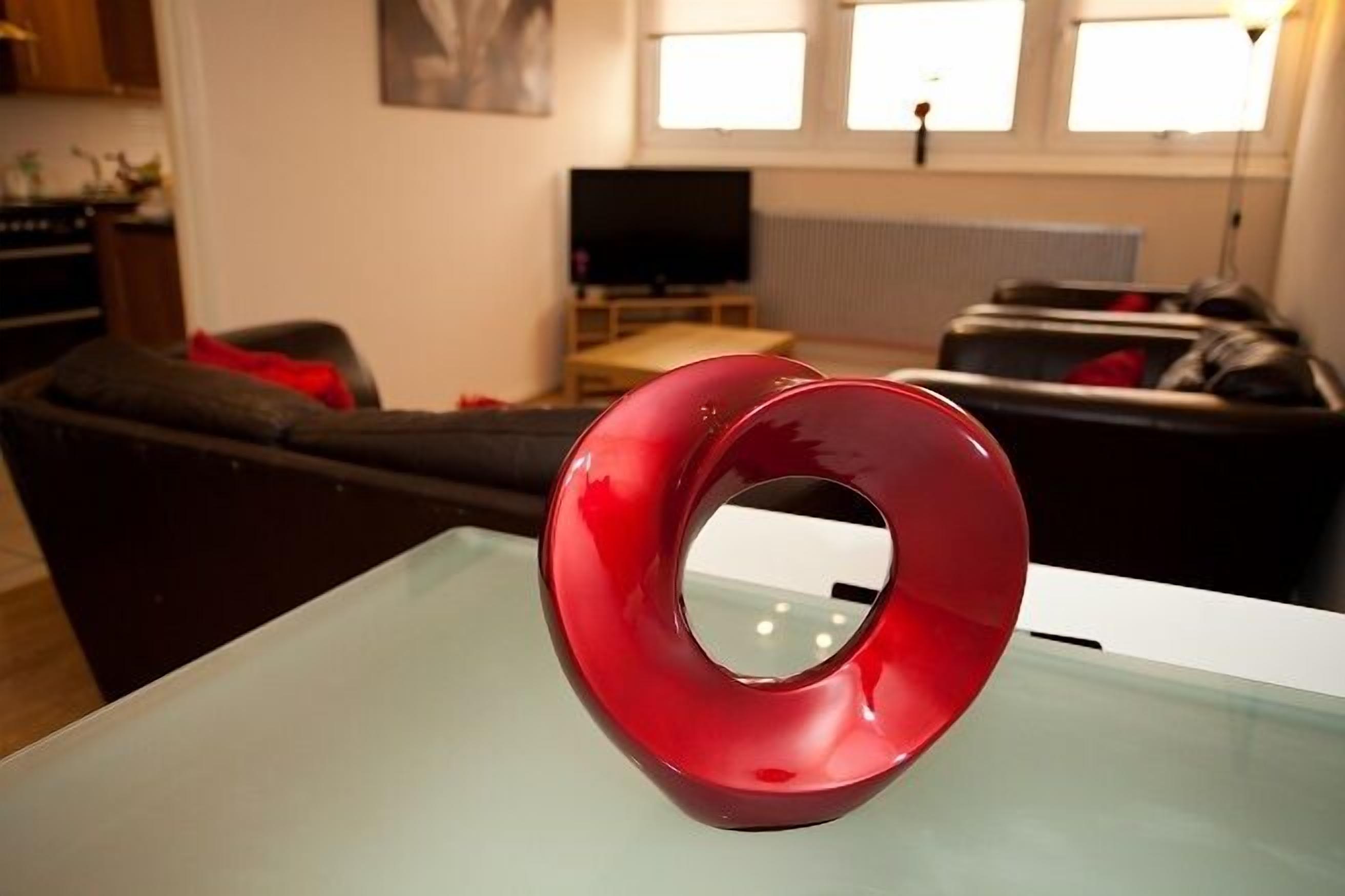 Un soggiorno moderno con un oggetto sferico rosso su un tavolino in vetro, un divano scuro, una televisione e un termosifone.