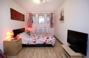Un dormitorio con cama, televisión, mesita de noche y ventana con cortinas.
